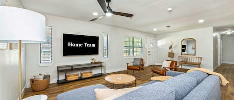 A living room with a large flat-screen TV, a ceiling fan, and a fireplace.