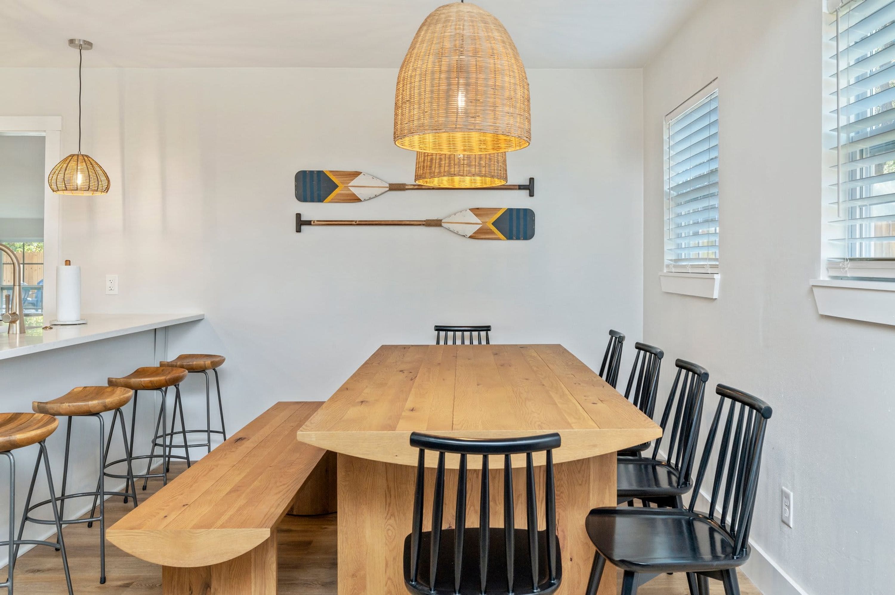 Un espace repas avec une table en bois, des chaises noires et un luminaire suspendu.