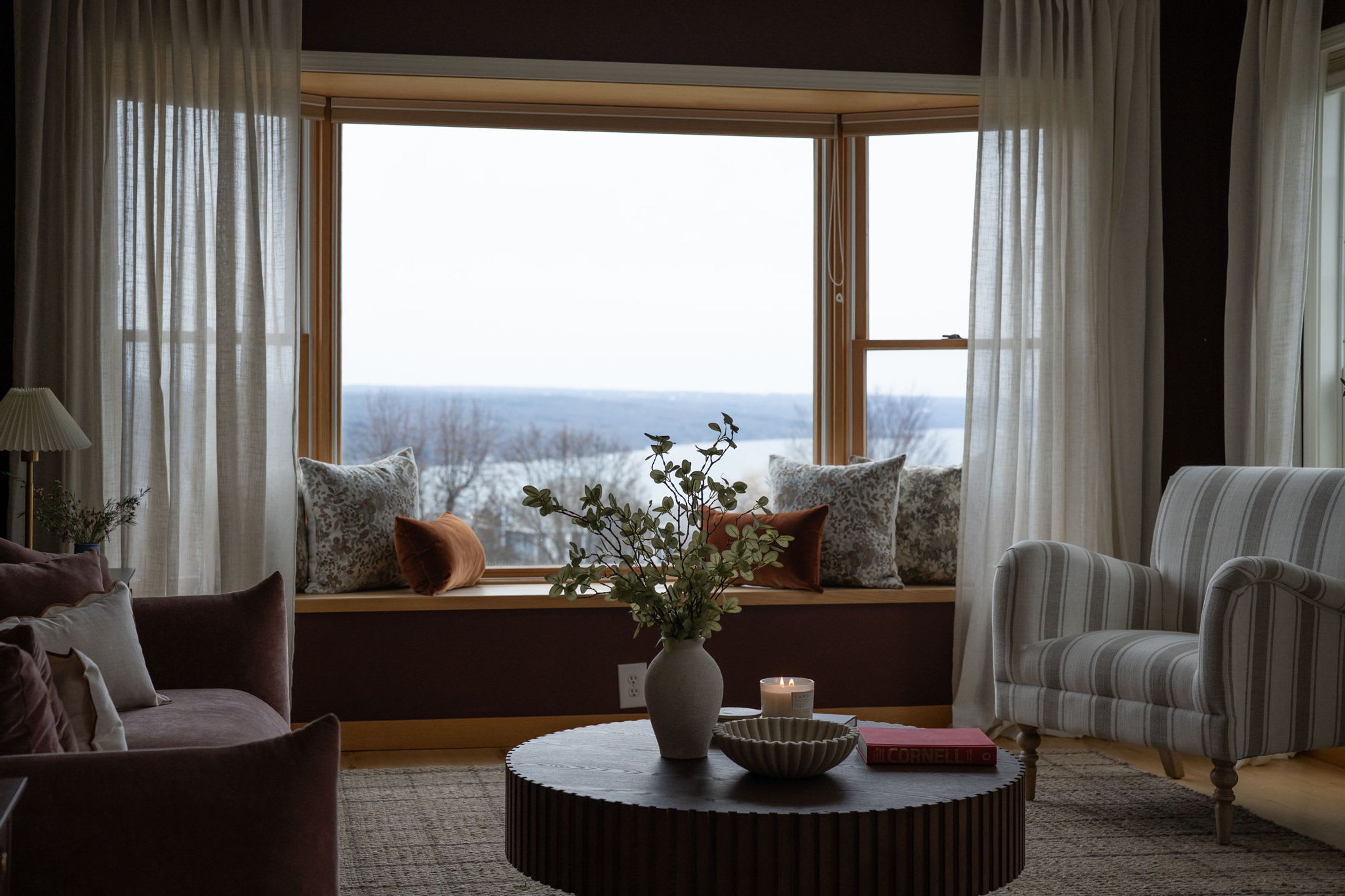 A living room with a large window, a round coffee table, and a view of a snowy landscape.