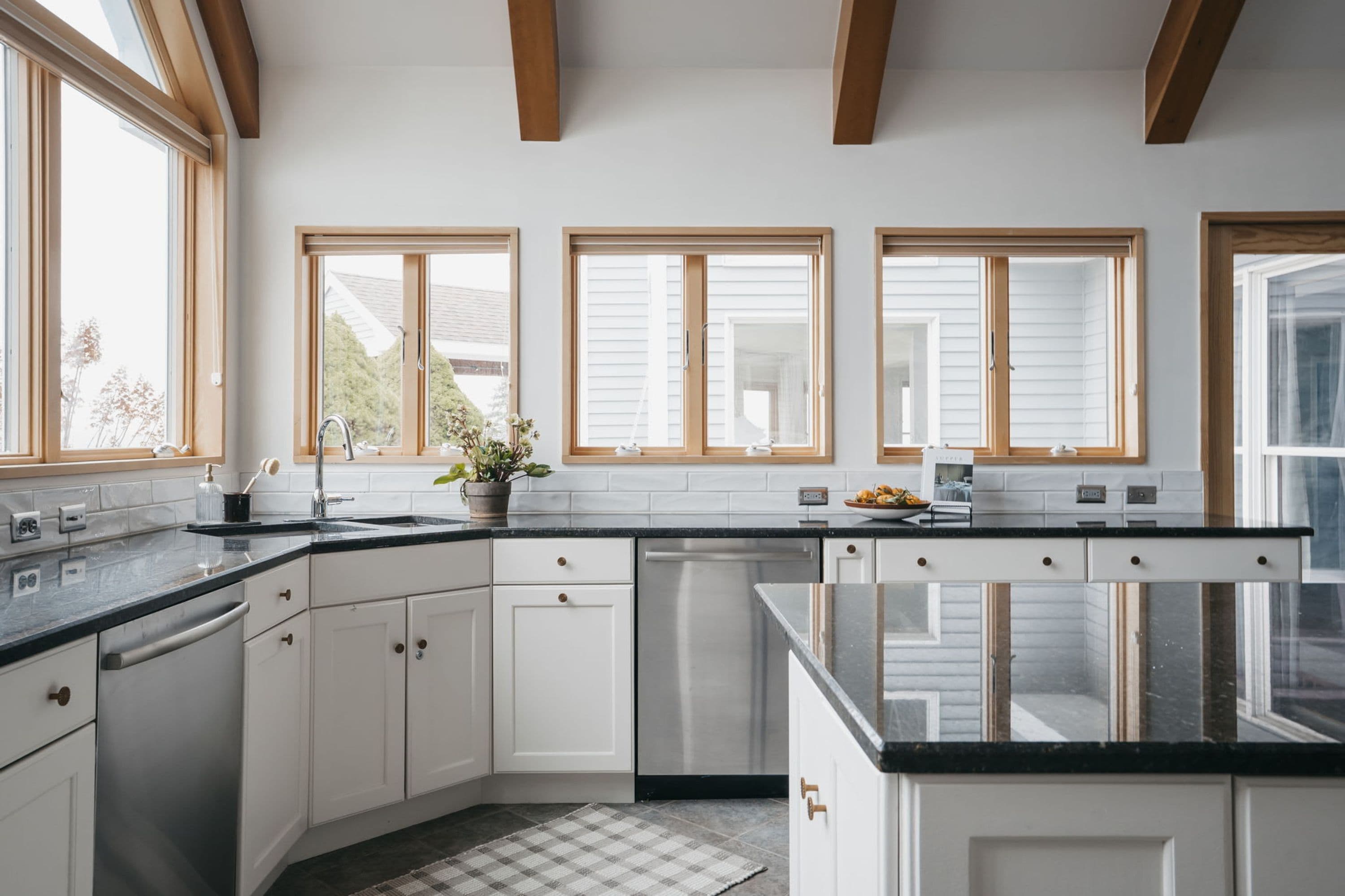 A modern kitchen with white cabinets, black countertops, and wooden beams on the ceiling.
