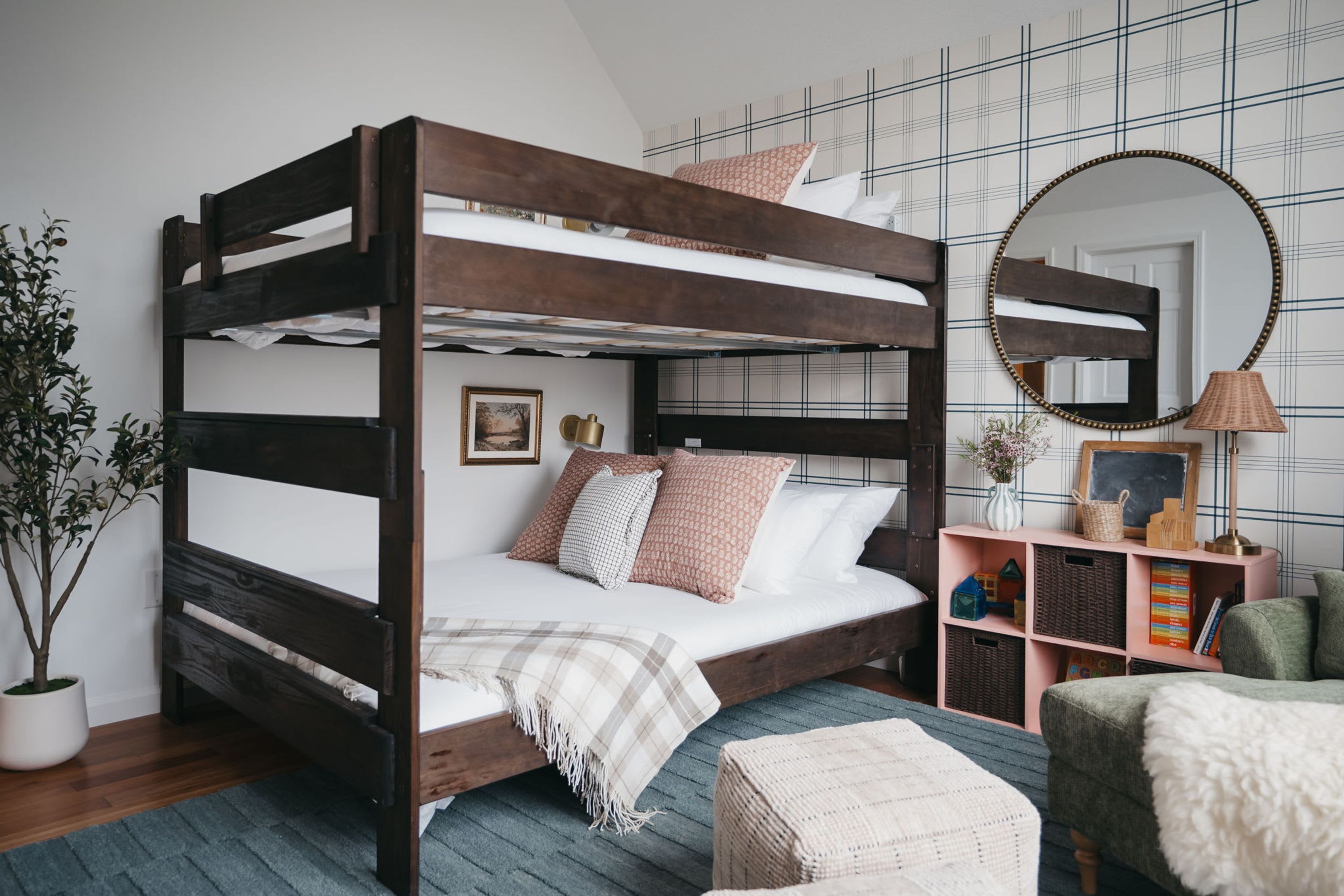 Un lit superposé avec une structure en bois, une table de chevet avec une lampe, un miroir et une petite étagère avec des livres et des objets décoratifs.