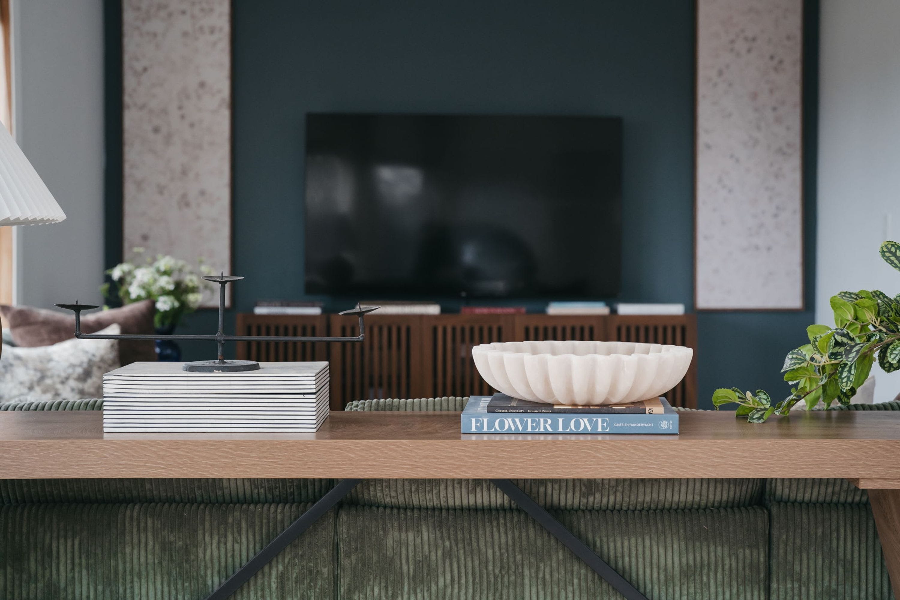 A modern living room with a flat-screen TV, a stack of books, a decorative bowl, and a potted plant.