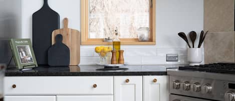 Una cocina con armarios blancos, encimera negra, estufa y ventana con vista a árboles.
