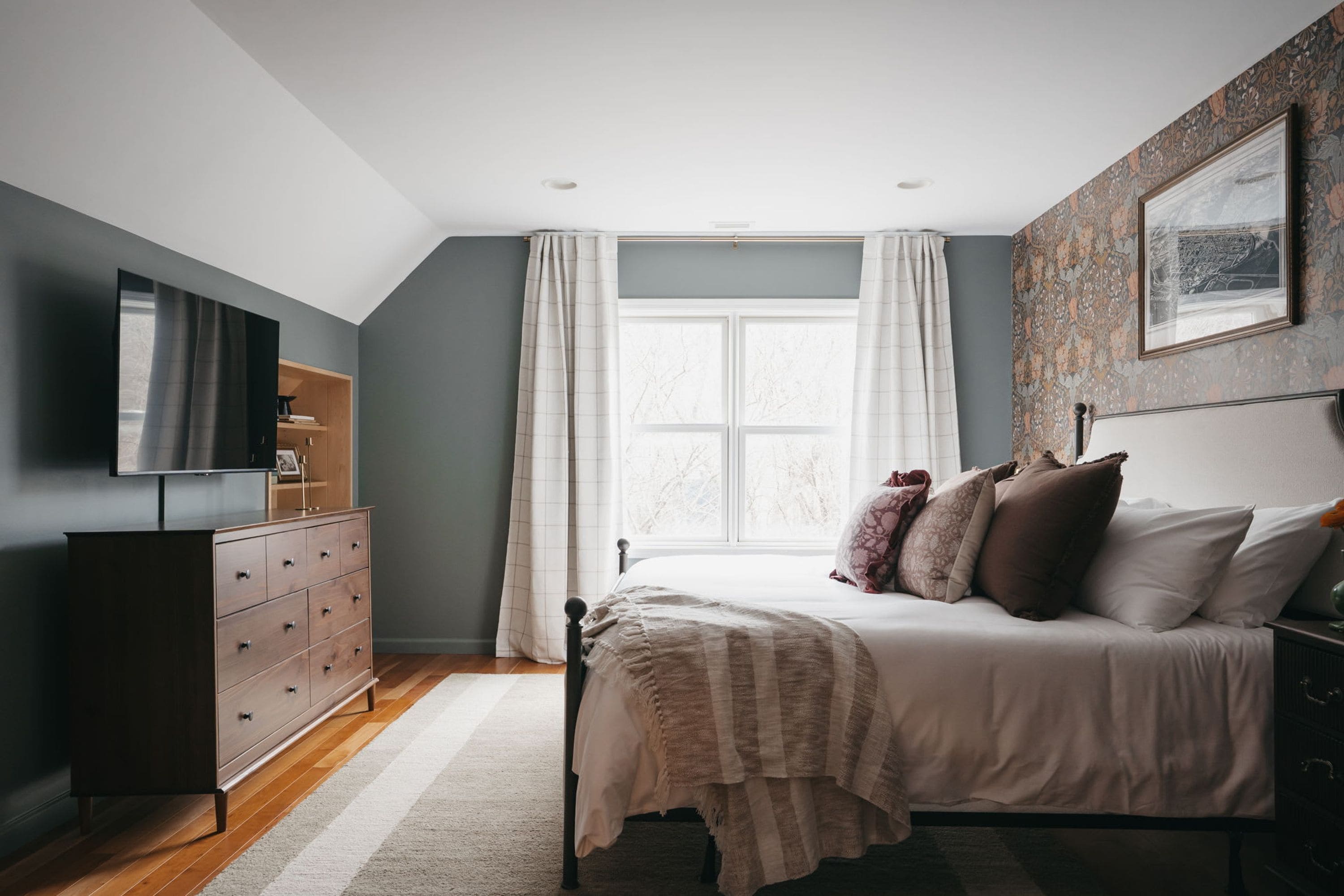 A bedroom with a bed, a dresser, a television, and a window with curtains.