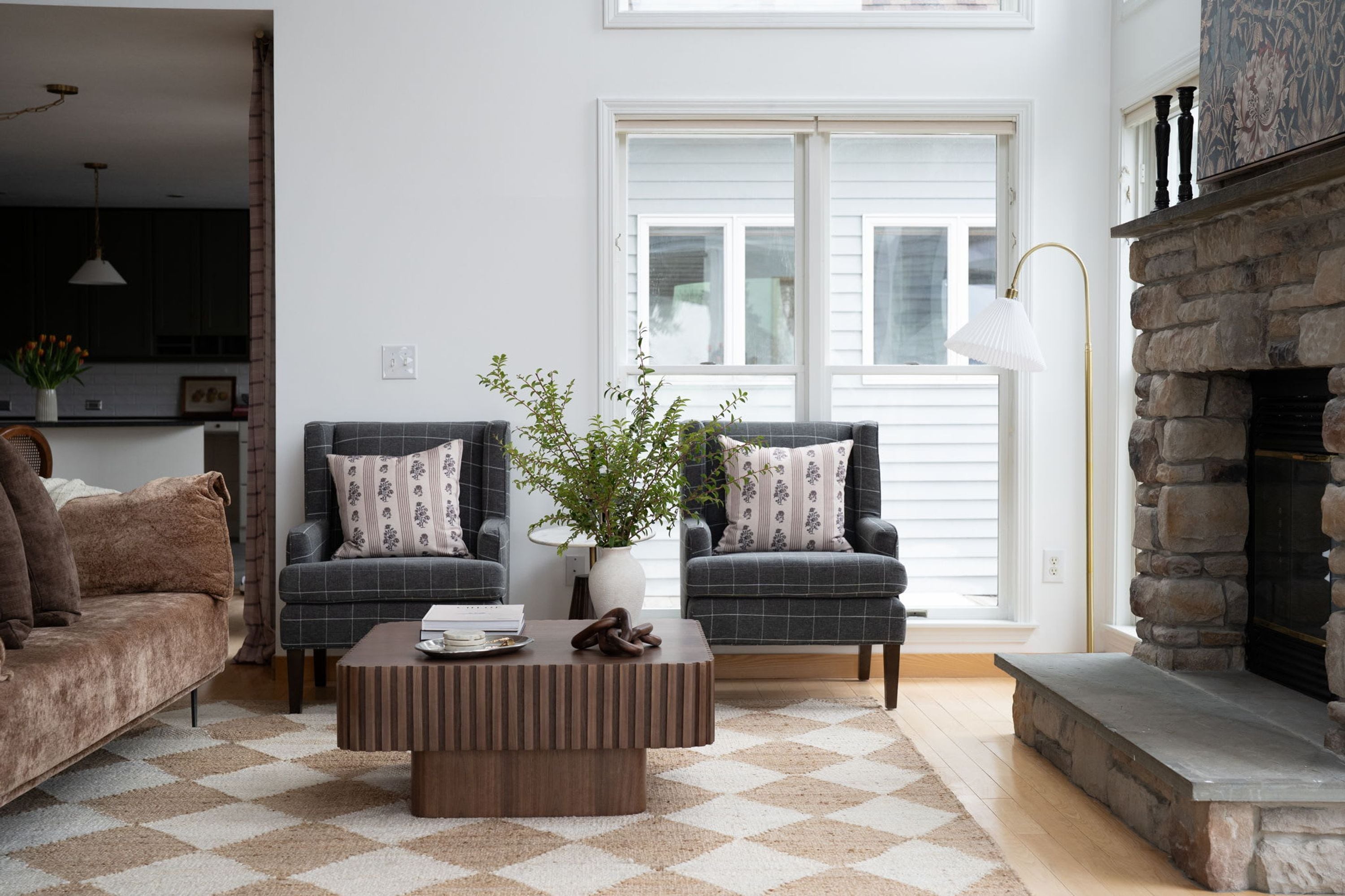 A living room with two armchairs, a coffee table, a fireplace, and a large window.