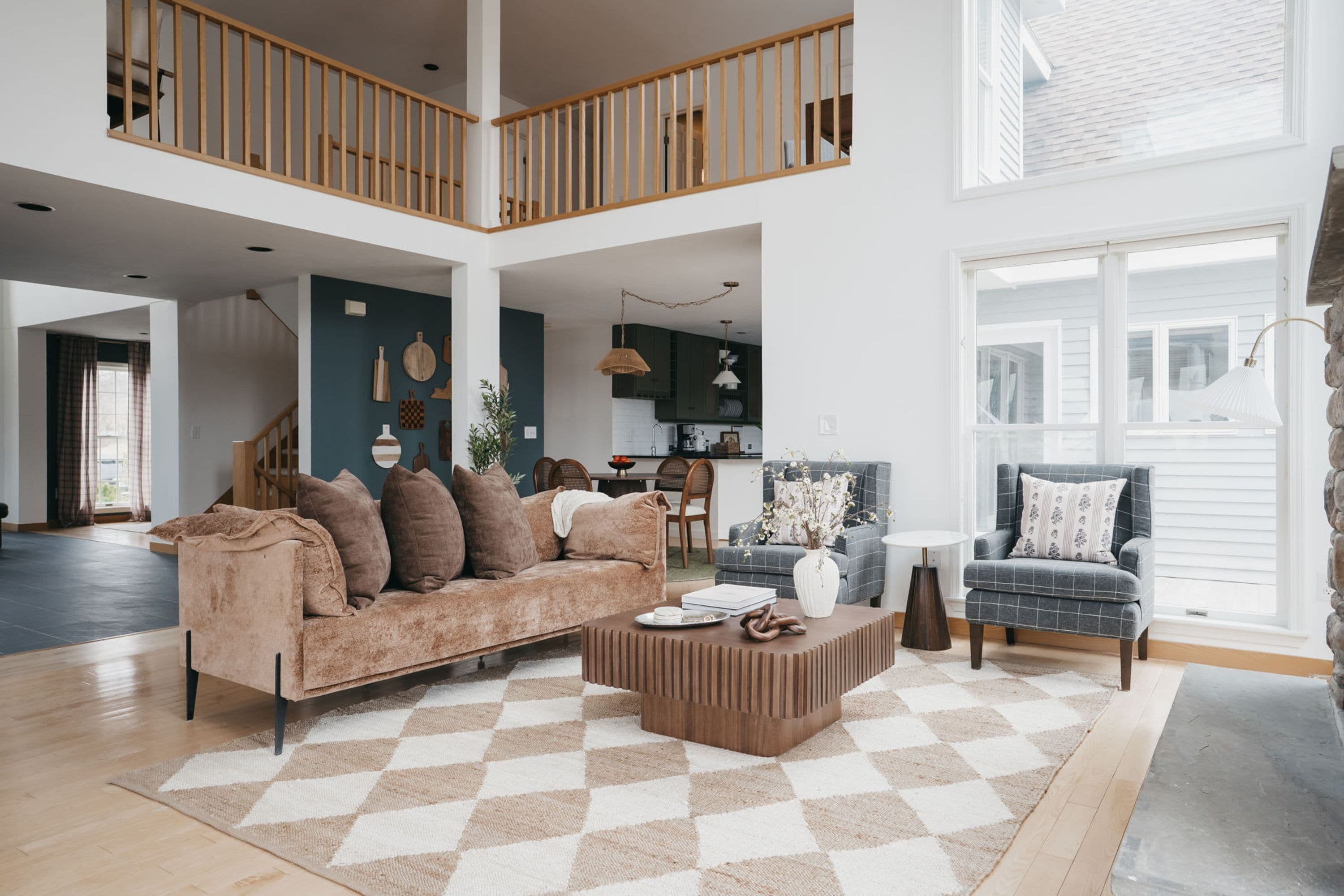 A spacious living area with a high ceiling, a checkered rug, a sofa, a coffee table, and a view of the kitchen and dining area.