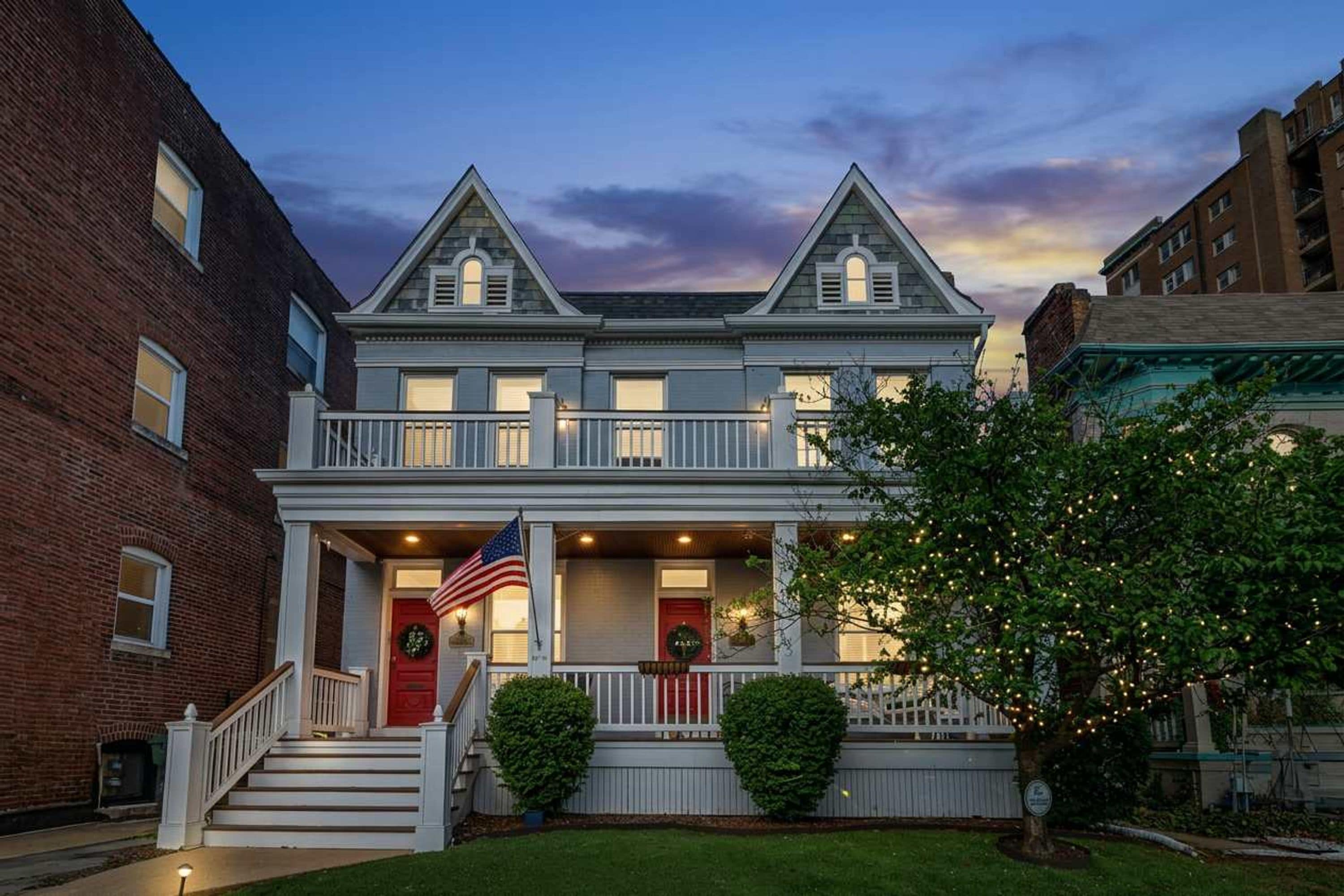 A two-story house with a front porch, a flag, and a well-maintained lawn.