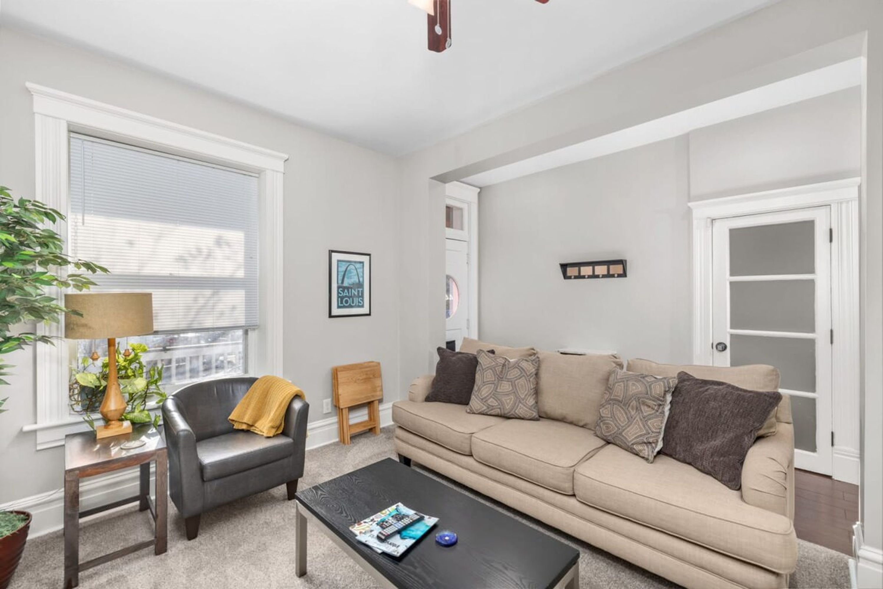 A living room with a sofa, a coffee table, a lamp, a small wooden stool, and a potted plant.