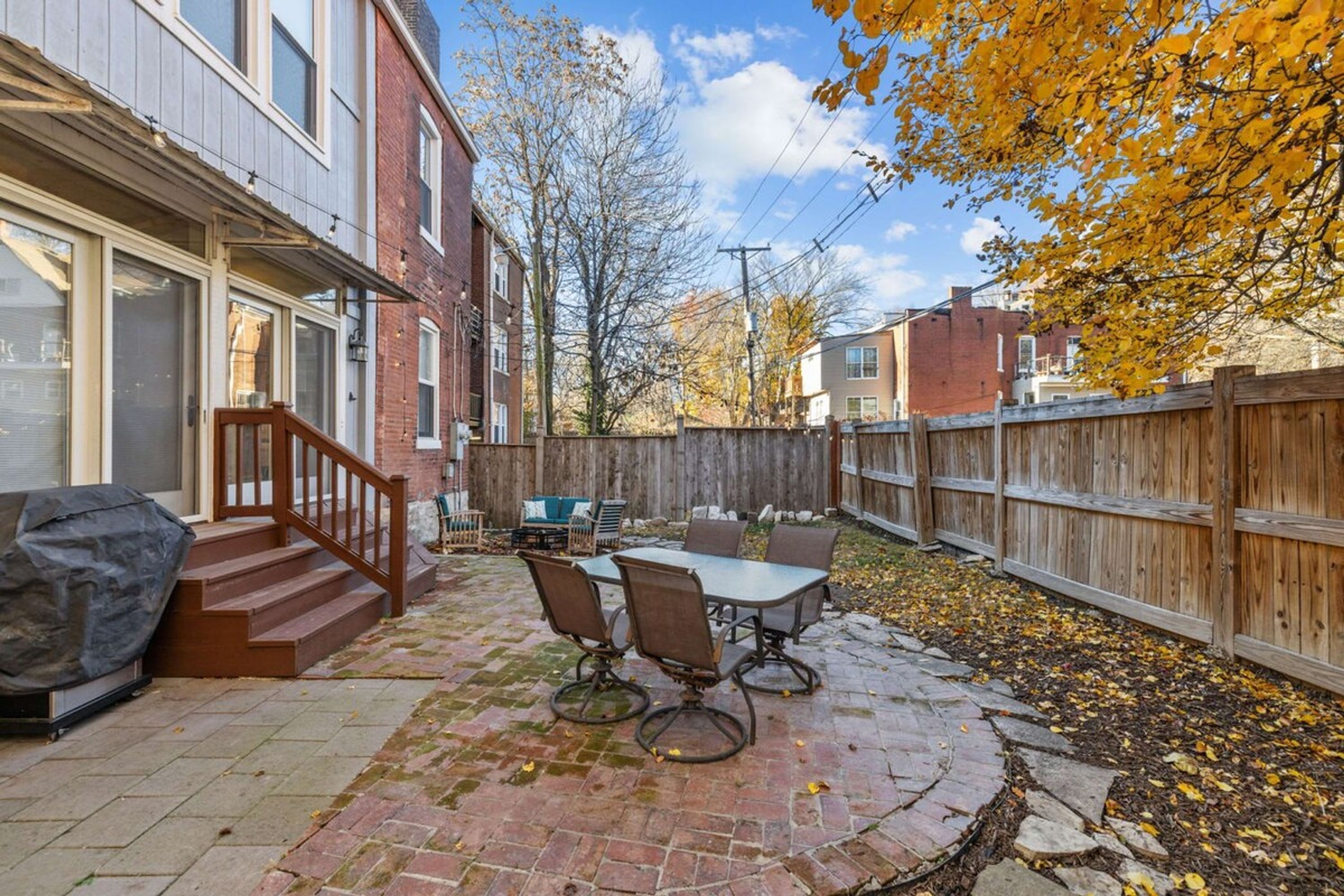 A patio with a table and chairs, a covered grill, and a wooden fence.