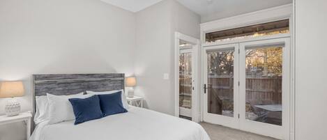 Un dormitorio con cama, mesitas de noche, ventilador de techo y puerta corrediza de vidrio que da a un patio exterior.