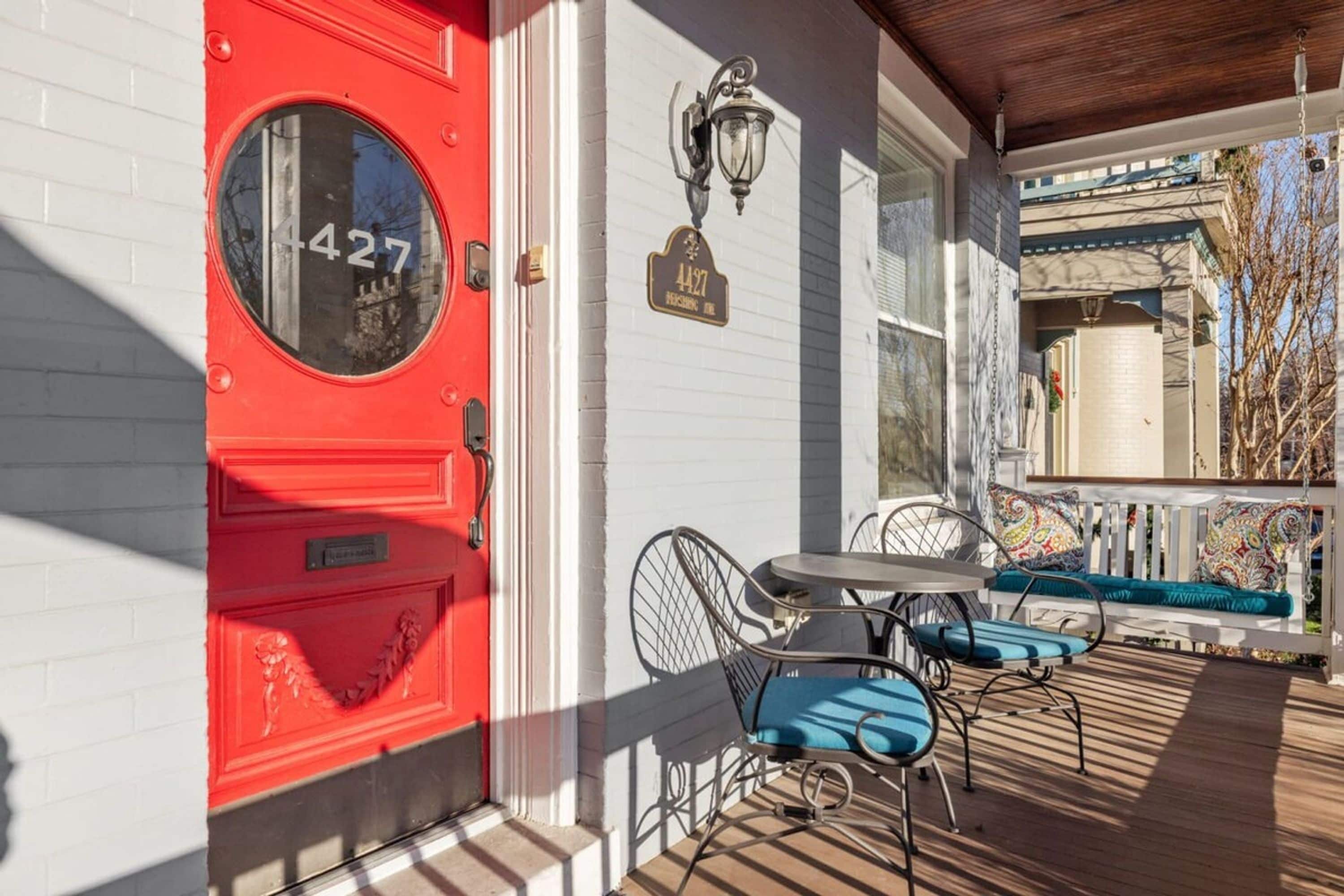 A red door with a round window, a mailbox, a street lamp, and a porch with a table and chairs.