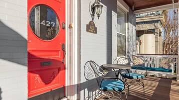 A red door with a round window, a mailbox, a street lamp, and a porch with a table and chairs.