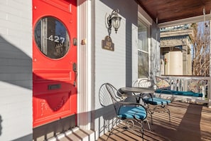 A red door with a round window, a mailbox, a street lamp, and a porch with a table and chairs. - Walk to Forest Park Fire Pit Porch Swing (St. Louis)