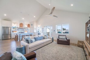 A spacious living area with a large sofa, a brown armchair, and a dining area with a kitchen in the background. - Glory Daze Private Pool Ice Maker EV Charger (Port Aransas)