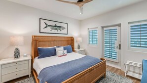 A bedroom with a bed, nightstands, a ceiling fan, a window with blinds, and a wall-mounted picture. - Glory Daze Private Pool Ice Maker EV Charger (Port Aransas)