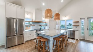 A modern kitchen with stainless steel appliances, a large island with bar stools, and large windows offering views. - Glory Daze Private Pool Ice Maker EV Charger (Port Aransas)