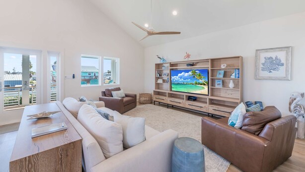 A spacious living room with a large flat-screen TV, comfortable seating, and a view of the outdoors. - Glory Daze Private Pool Ice Maker EV Charger (Port Aransas)