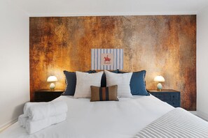 Habitación de hotel con una cama grande, dos mesitas de noche y una pared con textura.