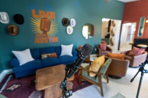 Ein Mikrofon auf einem Ständer in einem Raum mit einem blauen Sofa, einem Couchtisch und einer Wand mit dem Schriftzug 'LIVE AUSTRIN'.