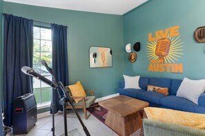 Una sala de estar con un sofá azul, una mesa de centro, una silla, un soporte para micrófono y una pared con la obra 'LIVE FROM AUSTIN'.