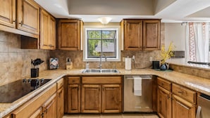 A kitchen with wooden cabinets, a stainless steel sink, and a dishwasher. - The Haven on Twisted Wood 4BR 3BA Sleeps 12 (San Antonio)
