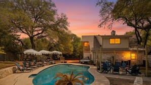 A swimming pool with lounge chairs and umbrellas, surrounded by trees and a stone wall. - The Haven on Twisted Wood 4BR 3BA Sleeps 12 (San Antonio)