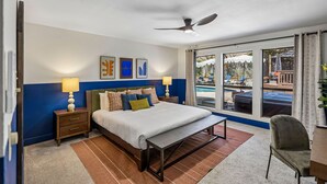 A hotel room with a bed, bedside tables, a desk, a chair, a window with a view of a pool, and ceiling fans. - The Haven on Twisted Wood 4BR 3BA Sleeps 12 (San Antonio)