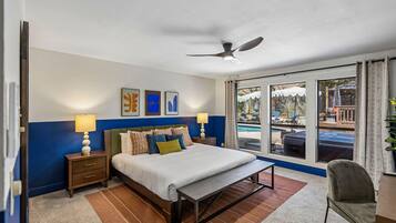 Una habitación de hotel con cama, mesitas de noche, escritorio, silla, ventana con vistas a una piscina y ventiladores de techo.