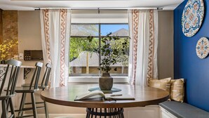 Ein Essbereich mit einem runden Tisch, Stühlen, einer Vase mit Blumen und Blick auf ein Haus durch das Fenster.
