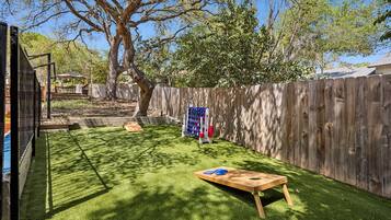 Un patio con césped artificial, una mesa de juego de madera y una valla de madera.