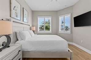 A bedroom with a bed, bedside tables, a lamp, a TV, and windows with blinds. - Luxury Waterfront 4Br Private Heated Pool Hot Tub (St. Petersburg)