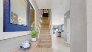 A hallway with a wooden staircase, a potted plant, and a small table with a decorative item. - Disney Min Away - Pool Patio Playground (Kissimmee)