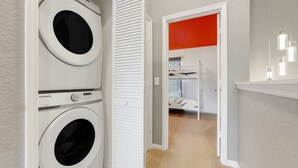 A laundry room with two front-loading washing machines, a white door leading to a room with a bed, and a bright red accent wall. - Disney Min Away - Pool Patio Playground (Kissimmee)