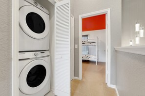 A laundry room with two front-loading washing machines, a white door leading to a room with a bed, and a bright red accent wall. - Disney Min Away - Pool Patio Playground (Kissimmee)