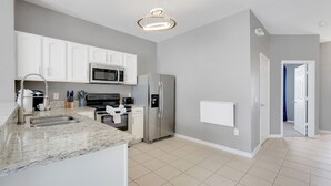 A modern kitchen with white cabinets, stainless steel appliances, and a marble countertop. - Disney Min Away - Pool Patio Playground (Kissimmee)