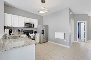 A modern kitchen with white cabinets, stainless steel appliances, and a marble countertop. - Disney Min Away - Pool Patio Playground (Kissimmee)