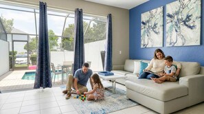 A family in a modern living room with a pool view, a sofa, and abstract art on the wall. - Disney Min Away - Pool Patio Playground (Kissimmee)