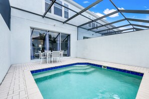 A swimming pool with a tiled edge, a patio with chairs, and a glass door leading to an interior space. - Disney Min Away - Pool Patio Playground (Kissimmee)