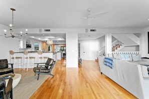 A spacious living area with a wooden floor, a sofa, a dining area with white chairs, and a kitchen in the background. - Walks on the Shores Private Beach Front Access (Indian Shores)