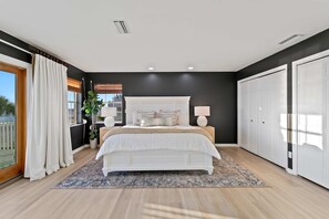 A bedroom with a large bed, two bedside lamps, a window with blinds, a potted plant, and a view of the outdoors. - Walks on the Shores Private Beach Front Access (Indian Shores)