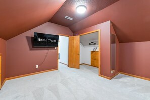 A room with a television displaying 'Home Team,' a wooden door, and a closet with a hanger. - 6 Br Sleeps 20 I Sauna Theater Putt Putt Hot Tub (Asheville)