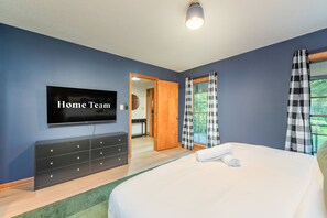 Un dormitorio con cama, cómoda, televisor y ventana con cortinas.