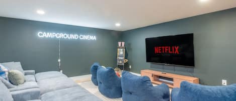 A modern living room with a large flat-screen TV, a couch, and bean bag chairs.