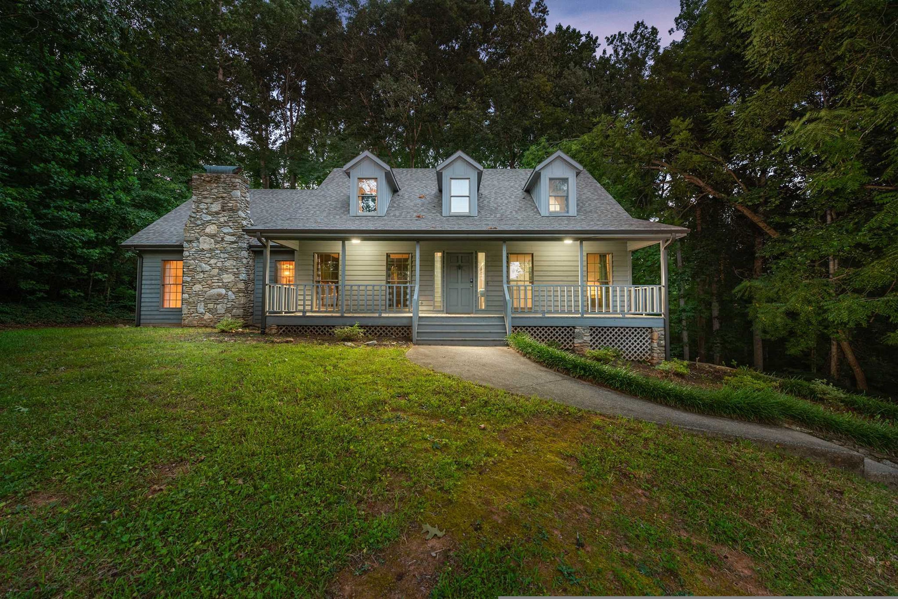 A two-story house with a stone chimney, a porch with railings, and a pathway leading to the entrance.