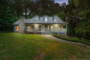 A two-story house with a stone chimney, a porch with railings, and a pathway leading to the entrance. - 6 Br Sleeps 20 I Sauna Theater Putt Putt Hot Tub (Asheville)