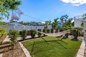Ein gepflegter Garten mit Hängematte, umzäunter Bereich und verschiedenen Pflanzen.