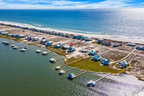 Vue aérienne d’une propriété côtière comprenant plusieurs bâtiments, une marina avec des bateaux et une plage.