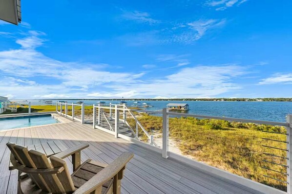 Une terrasse en bois avec une piscine, des chaises et une vue sur une étendue d’eau.