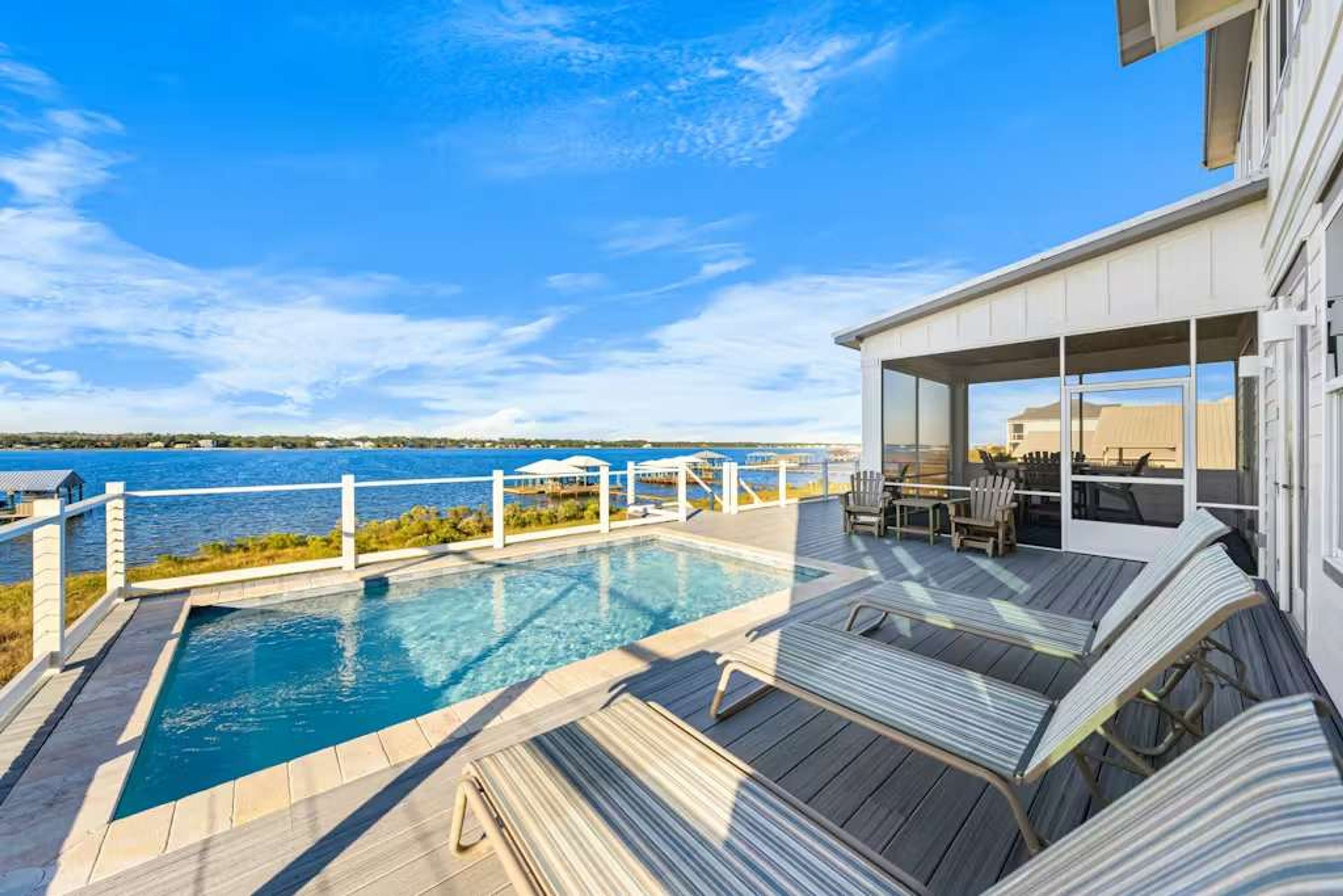 A pool area with a view of the sea, lounge chairs, and a covered seating area.