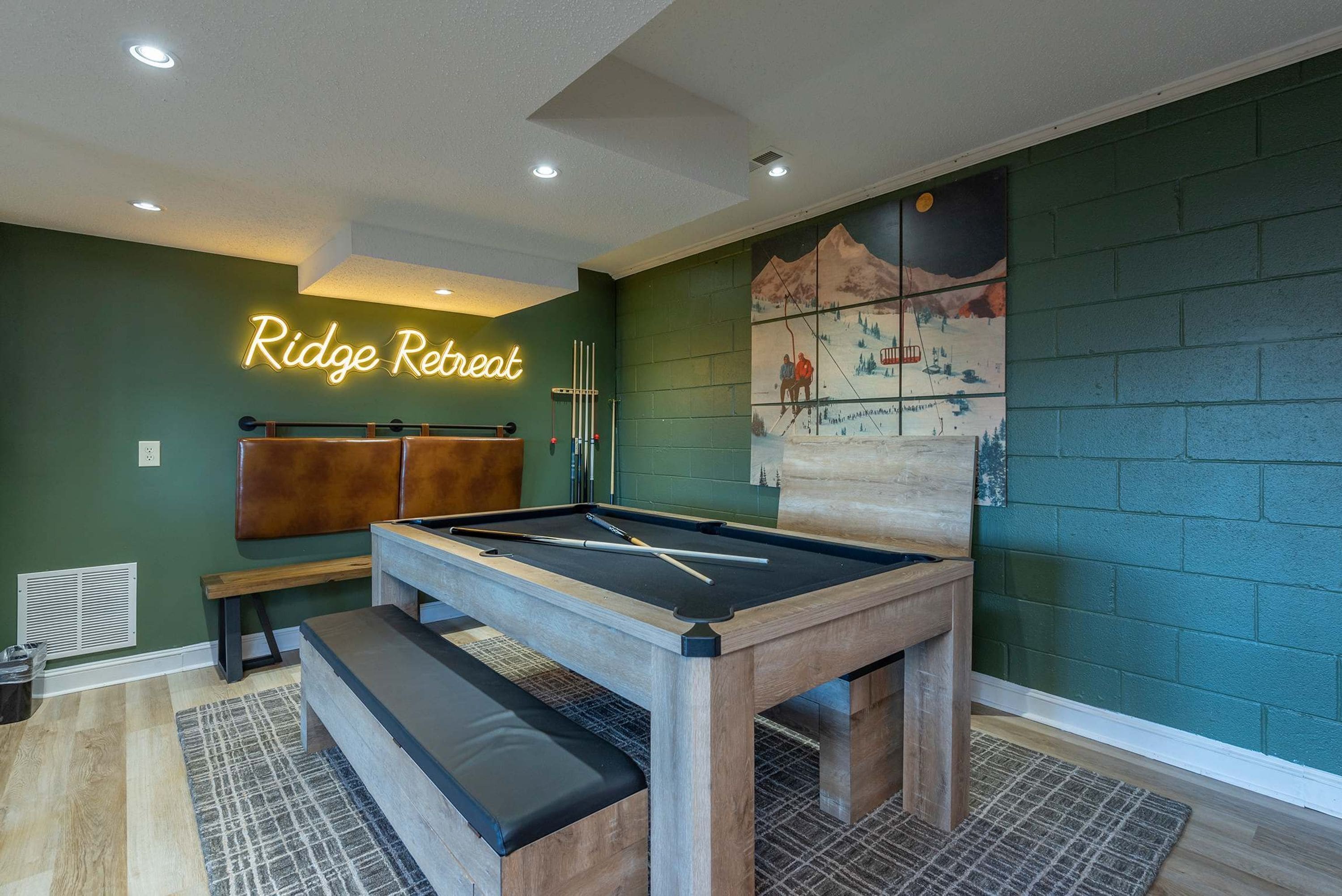A pool table with a neon sign reading 'Ridge Retreat' in a room with green walls and a mural.